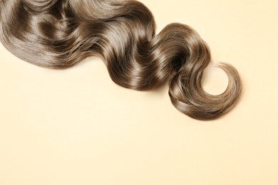 Image of Lock of shiny wavy hair on beige background, top view. Space for text