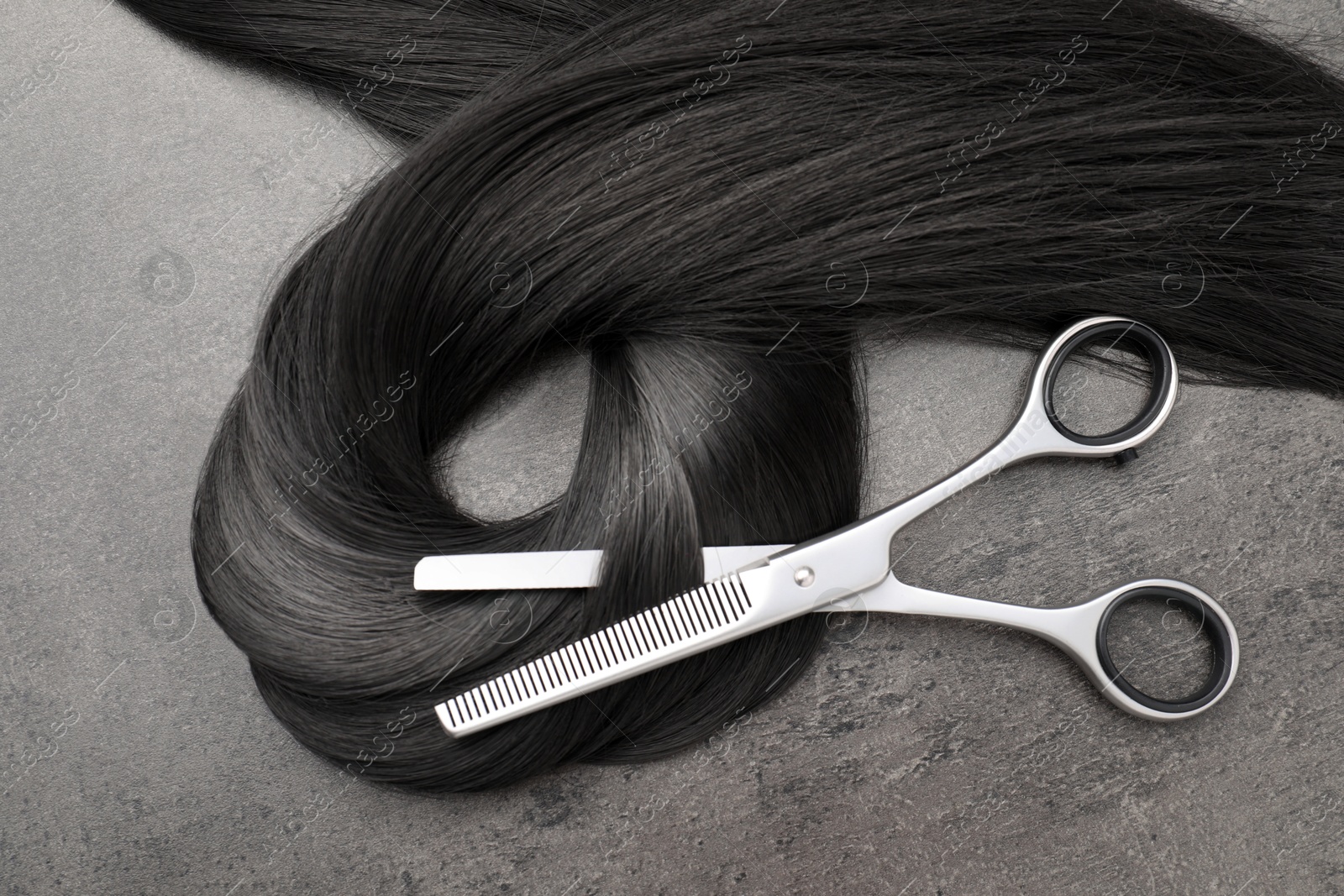 Black hair strand and professional scissors on grey surface, top view Image of Black hair strand and professional scissors on grey surface, top view