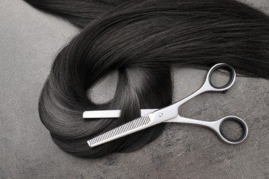 Image of Black hair strand and professional scissors on grey surface, top view
