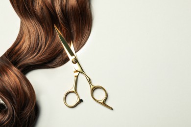 Image of Professional hairdresser scissors with brown hair strand on light grey background, top view. Space for text