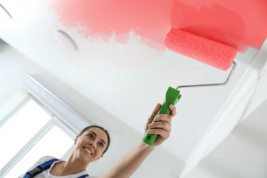Image of Happy woman painting ceiling with red dye indoors, low angle view