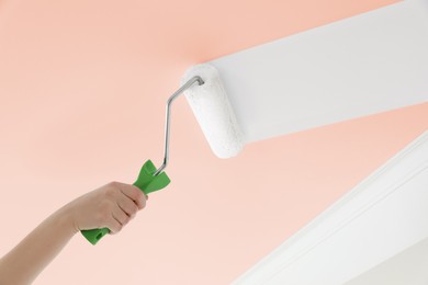 Image of Woman repainting pink ceiling with white dye, closeup. Low angle view