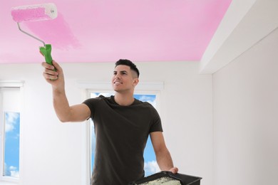Image of Man painting ceiling with pink dye indoors