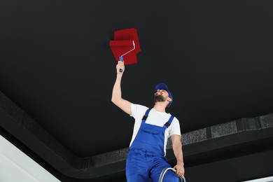 Image of Man repainting black ceiling with red dye indoors, low angle view
