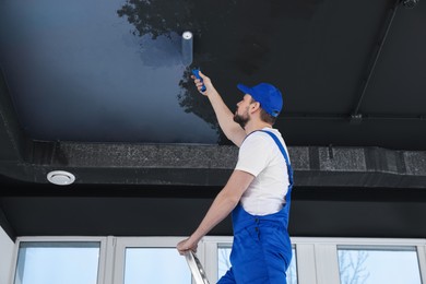 Image of Man repainting black ceiling with pastel blue dye indoors, low angle view