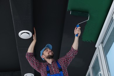 Image of Man repainting black ceiling with green dye indoors, low angle view