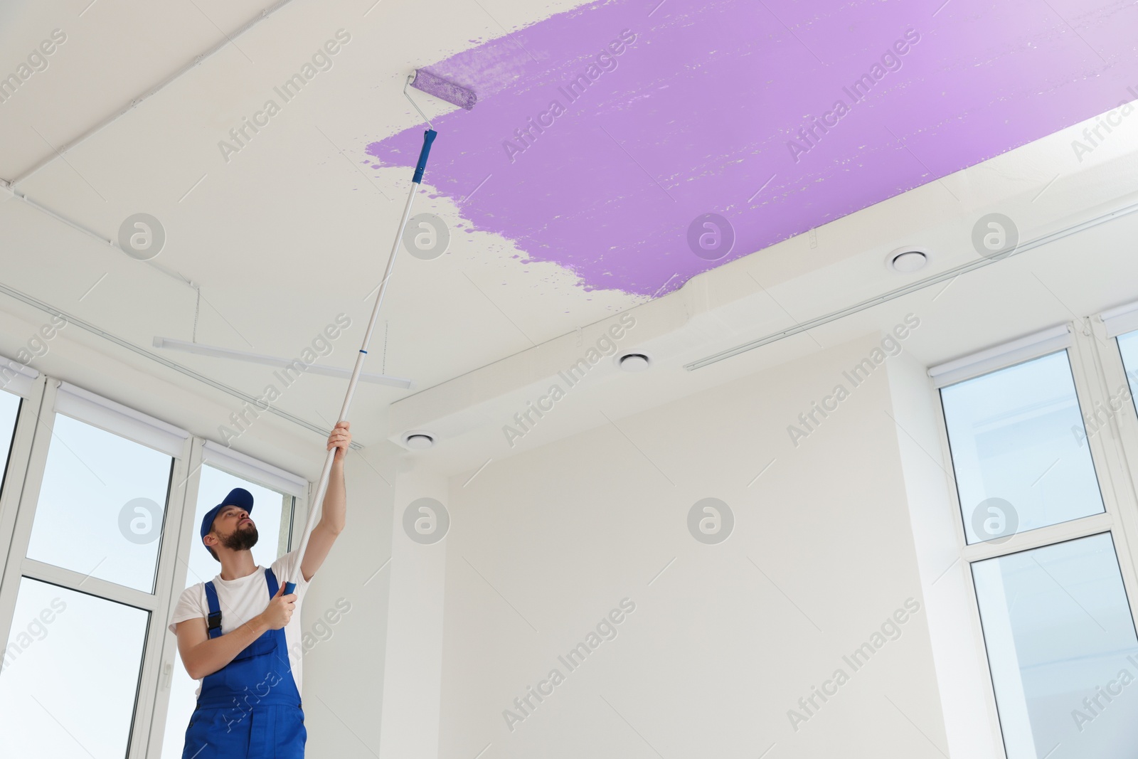 Man painting white ceiling with violet dye indoors, low angle view Image of Man painting white ceiling with violet dye indoors, low angle view