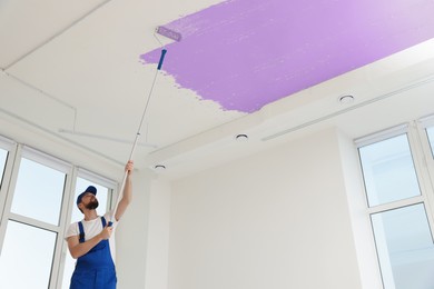 Image of Man painting white ceiling with violet dye indoors, low angle view