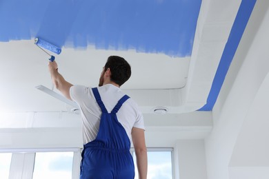 Image of Man painting white ceiling with blue dye indoors, low angle view