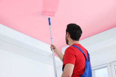 Image of Man painting ceiling with pink dye indoors, low angle view