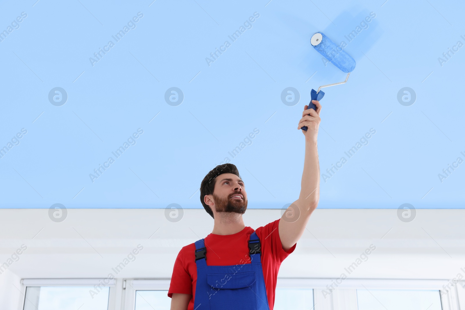 Man painting ceiling with light blue dye indoors, low angle view Image of Man painting ceiling with light blue dye indoors, low angle view