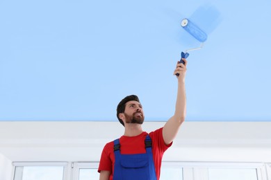Image of Man painting ceiling with light blue dye indoors, low angle view