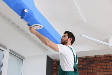 Image of Man painting white ceiling with blue dye indoors, low angle view