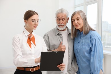 Photo of Smiling real estate agent with clipboard working with couple at home