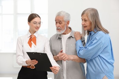 Photo of Smiling real estate agent with clipboard working with couple at home