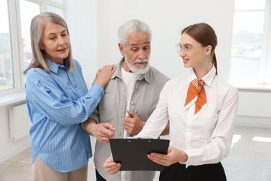 Photo of Smiling real estate agent with clipboard working with couple at home