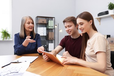 Photo of Real estate agent and couple with tablet at table in office