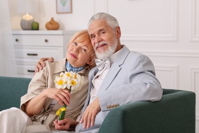 Photo of Lovely senior couple with bouquet of flowers on sofa at home