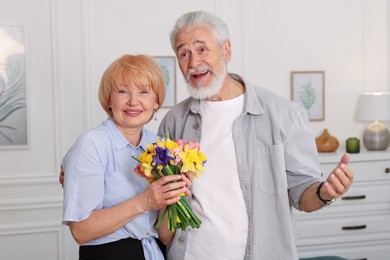 Photo of Lovely senior couple with bouquet of flowers at home