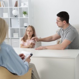 Photo of Father and daughter having consultation with psychologist in office, selective focus