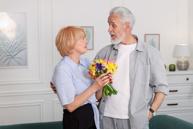 Photo of Lovely senior couple with bouquet of flowers at home
