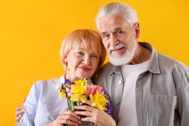 Photo of Lovely senior couple with bouquet of flowers on yellow background