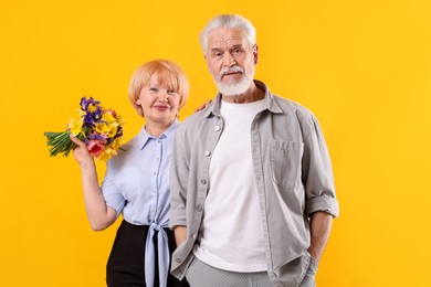 Photo of Lovely senior couple with bouquet of flowers on yellow background