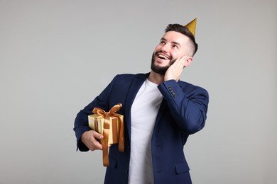 Photo of Happy Birthday. Handsome man with party hat and gift box on grey background