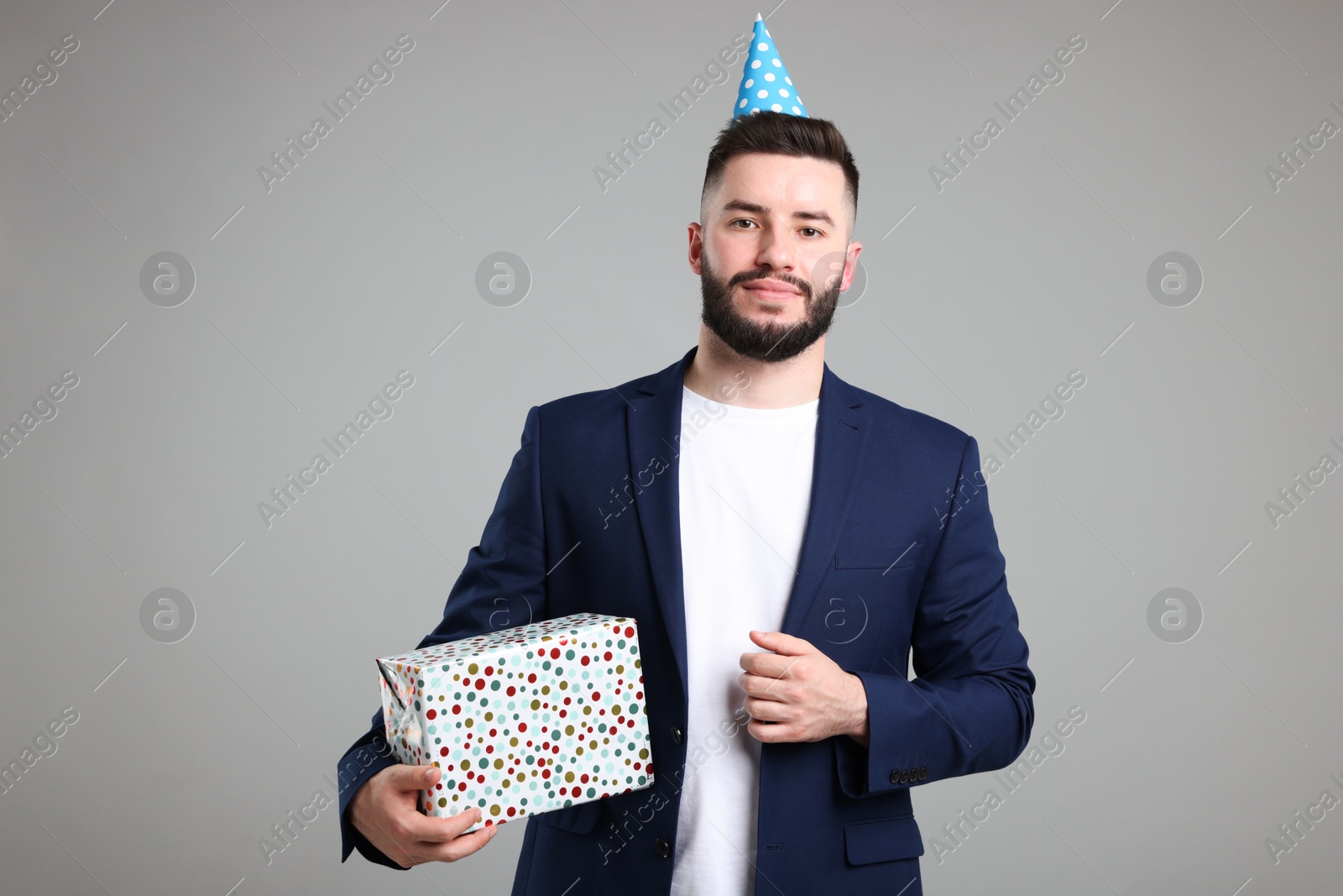 Happy Birthday. Handsome man with party hat and gift box on grey background Photo of Happy Birthday. Handsome man with party hat and gift box on grey background