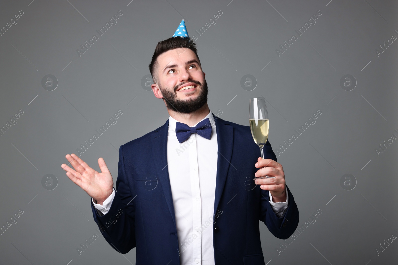 Happy Birthday. Handsome man with party hat and glass of champagne on grey background Photo of Happy Birthday. Handsome man with party hat and glass of champagne on grey background