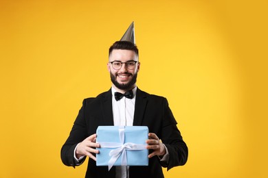 Photo of Happy Birthday. Handsome man with party hat and gift box on orange background