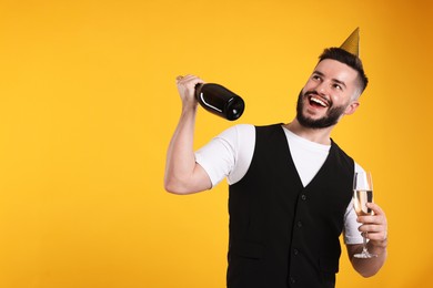 Photo of Happy Birthday. Handsome man with party hat and champagne on orange background, space for text
