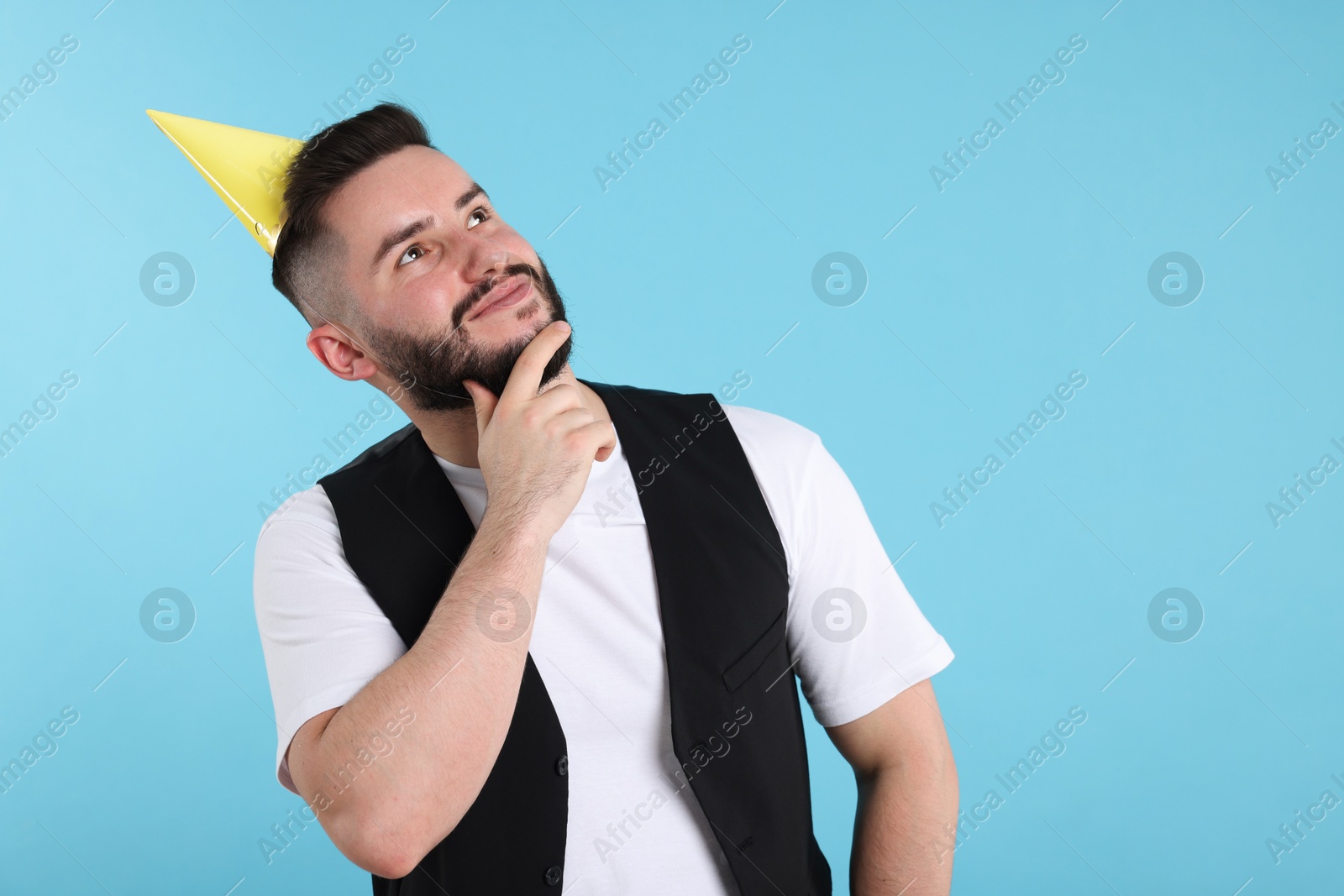Happy Birthday. Handsome man with party hat on light blue background, space for text Photo of Happy Birthday. Handsome man with party hat on light blue background, space for text