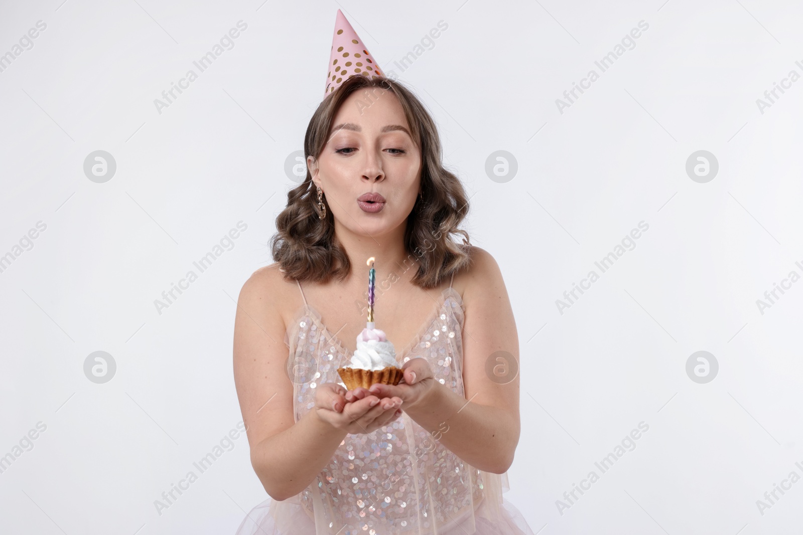 Birthday celebration. Woman blowing candle on cupcake against white background Photo of Birthday celebration. Woman blowing candle on cupcake against white background