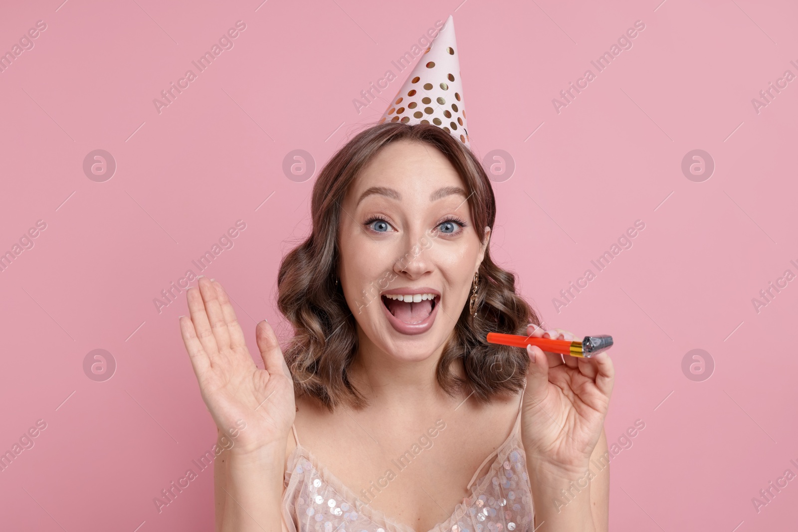 Birthday celebration. Woman with party horn on pink background Photo of Birthday celebration. Woman with party horn on pink background