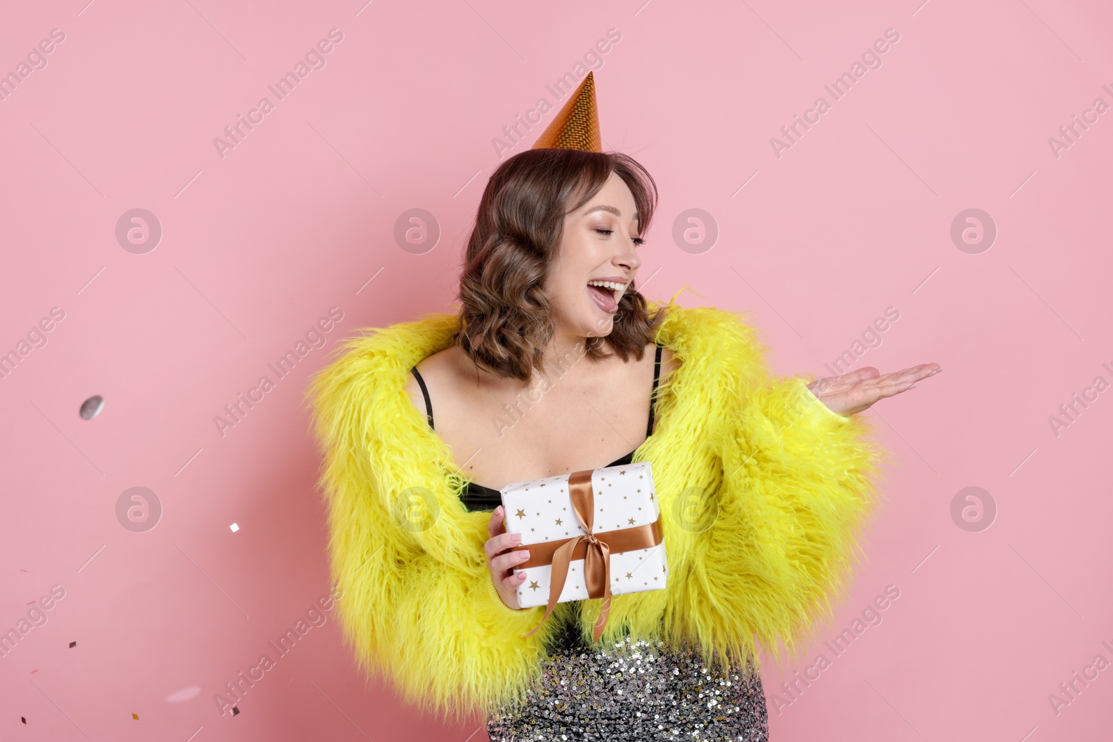 Birthday celebration. Woman with gift and confetti on pink background Photo of Birthday celebration. Woman with gift and confetti on pink background