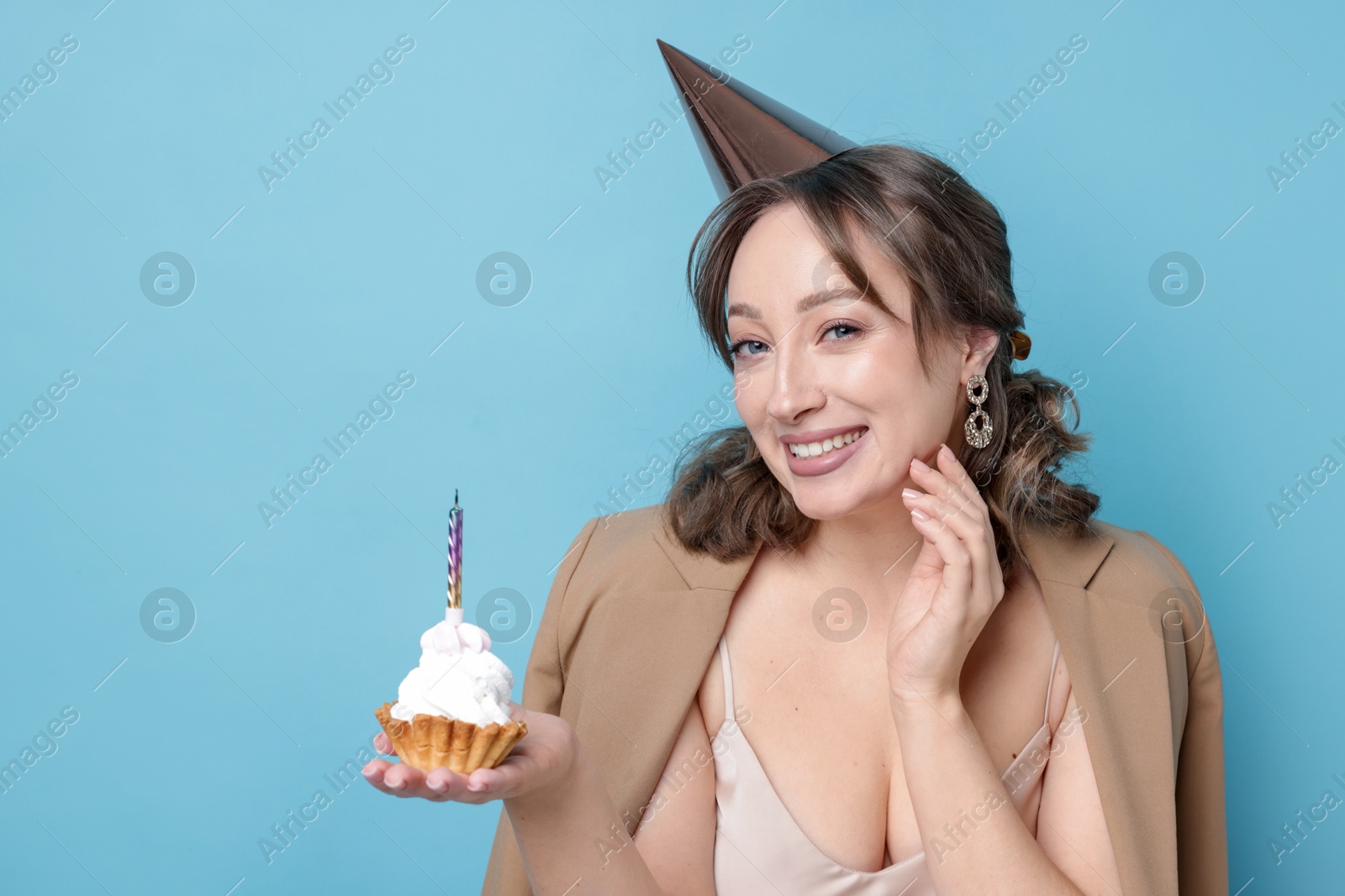 Birthday celebration. Woman with cupcake on light blue background Photo of Birthday celebration. Woman with cupcake on light blue background