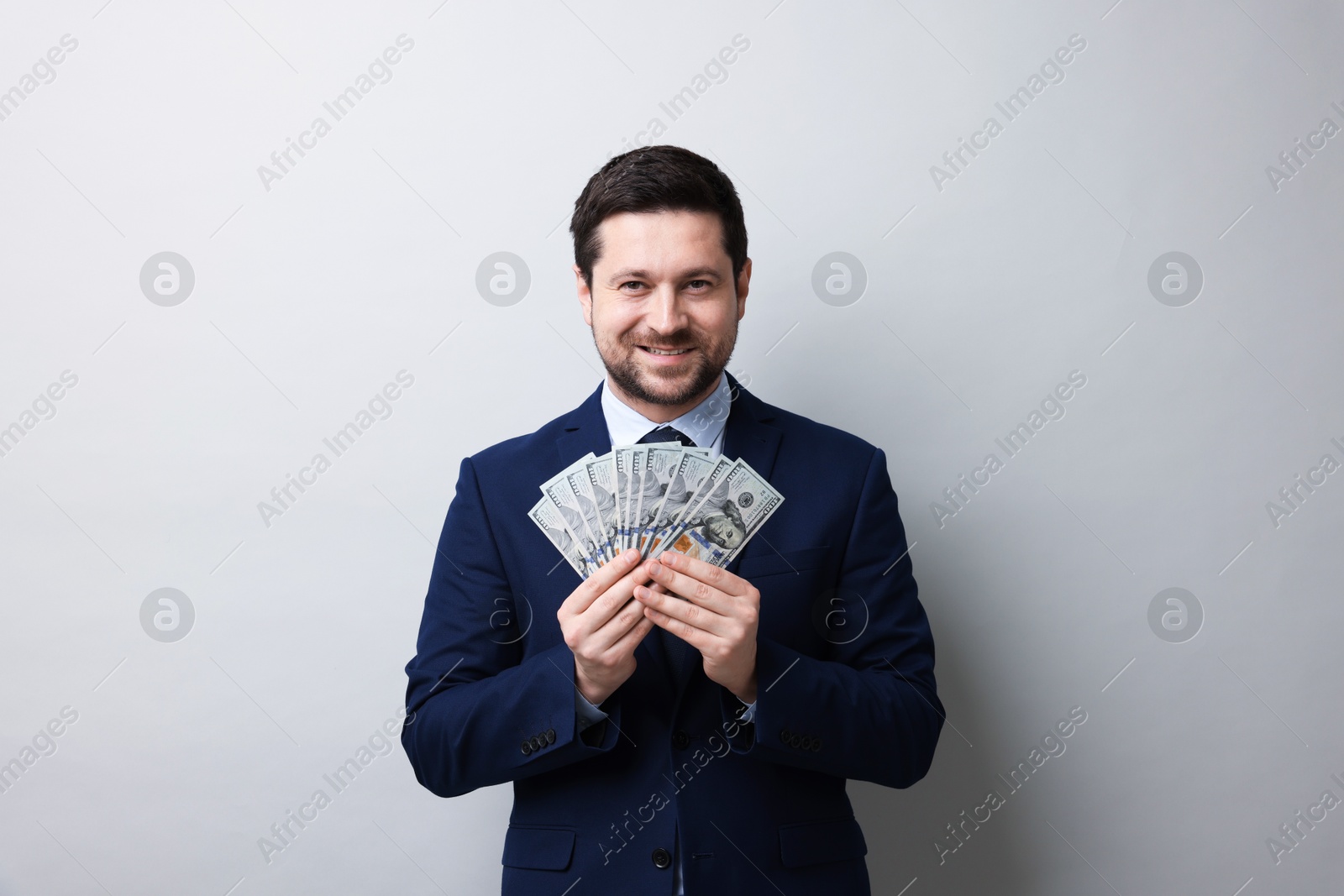 Happy greedy banker with dollar banknotes on grey background Photo of Happy greedy banker with dollar banknotes on grey background