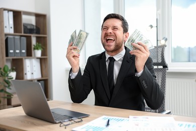 Photo of Happy greedy banker with dollar banknotes at table in office