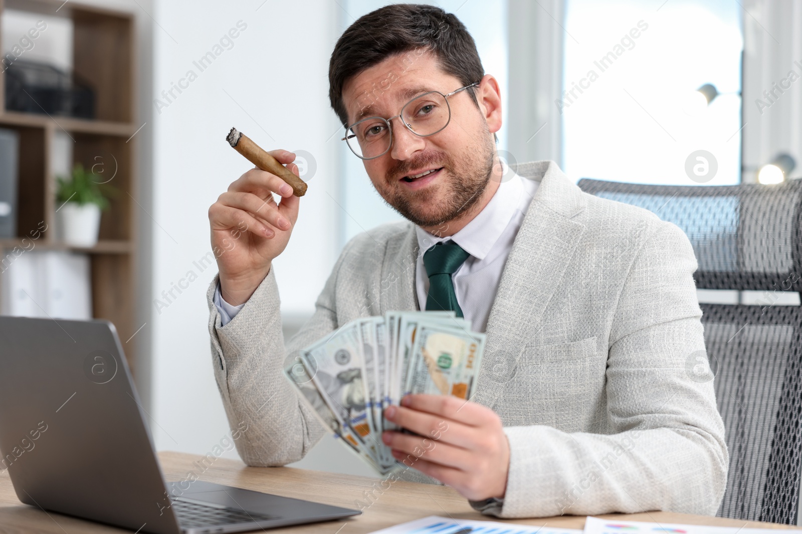Greedy banker with dollar banknotes and cigar at table in office Photo of Greedy banker with dollar banknotes and cigar at table in office