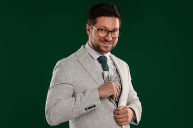 Photo of Happy greedy banker hiding money into inner pocket of suit on green background