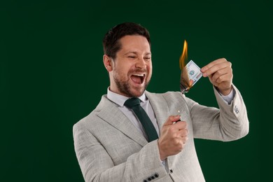 Photo of Emotional greedy banker with burning dollar banknote and lighter on green background