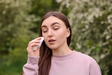 Photo of Woman with paper tissue suffering from seasonal pollen allergy near blossoming shrub on spring day