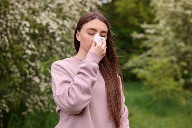 Photo of Woman with paper tissue suffering from seasonal pollen allergy near blossoming shrub on spring day