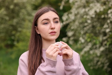 Photo of Woman with paper tissue suffering from seasonal pollen allergy near blossoming shrub on spring day