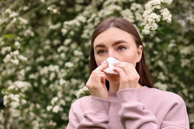 Photo of Woman with paper tissue suffering from seasonal pollen allergy near blossoming shrub on spring day, space for text