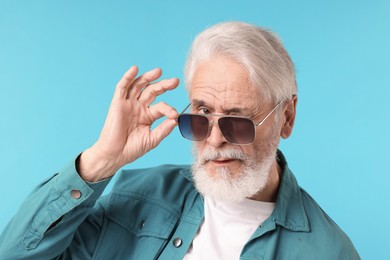 Photo of Elderly man in stylish sunglasses on light blue background