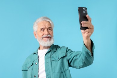 Photo of Elderly man taking selfie on light blue background