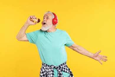 Photo of Elderly man in headphones with ice cream on orange background