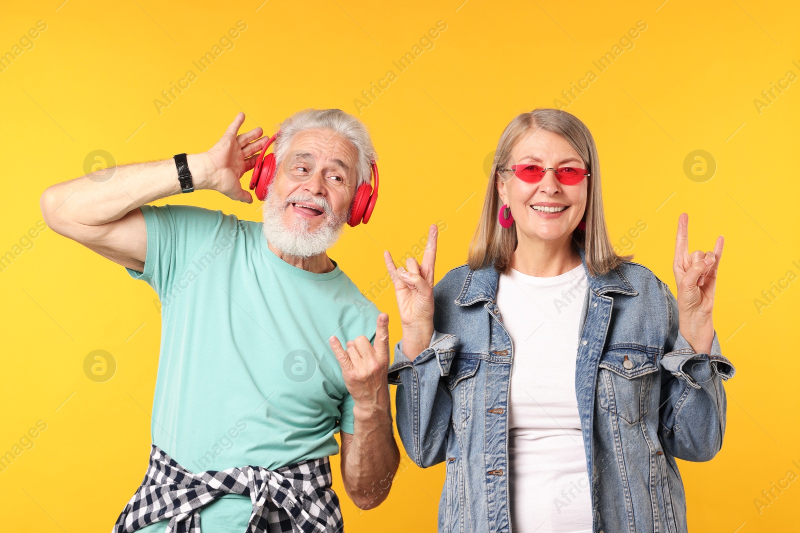 Senior couple in stylish outfits making rock gestures on orange background Photo of Senior couple in stylish outfits making rock gestures on orange background